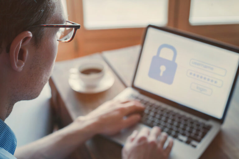 Man wearing glasses typing on a laptop with a login screen and padlock icon visible.
