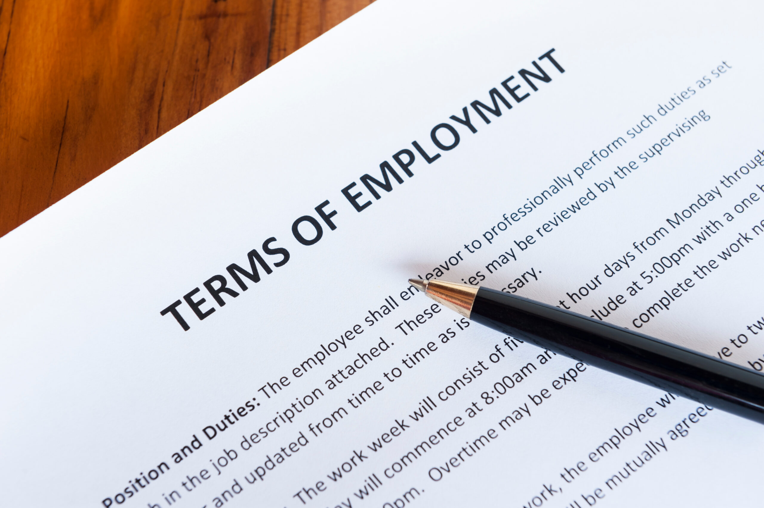 Close-up of a "Terms of Employment" document with a black pen on a wooden surface.